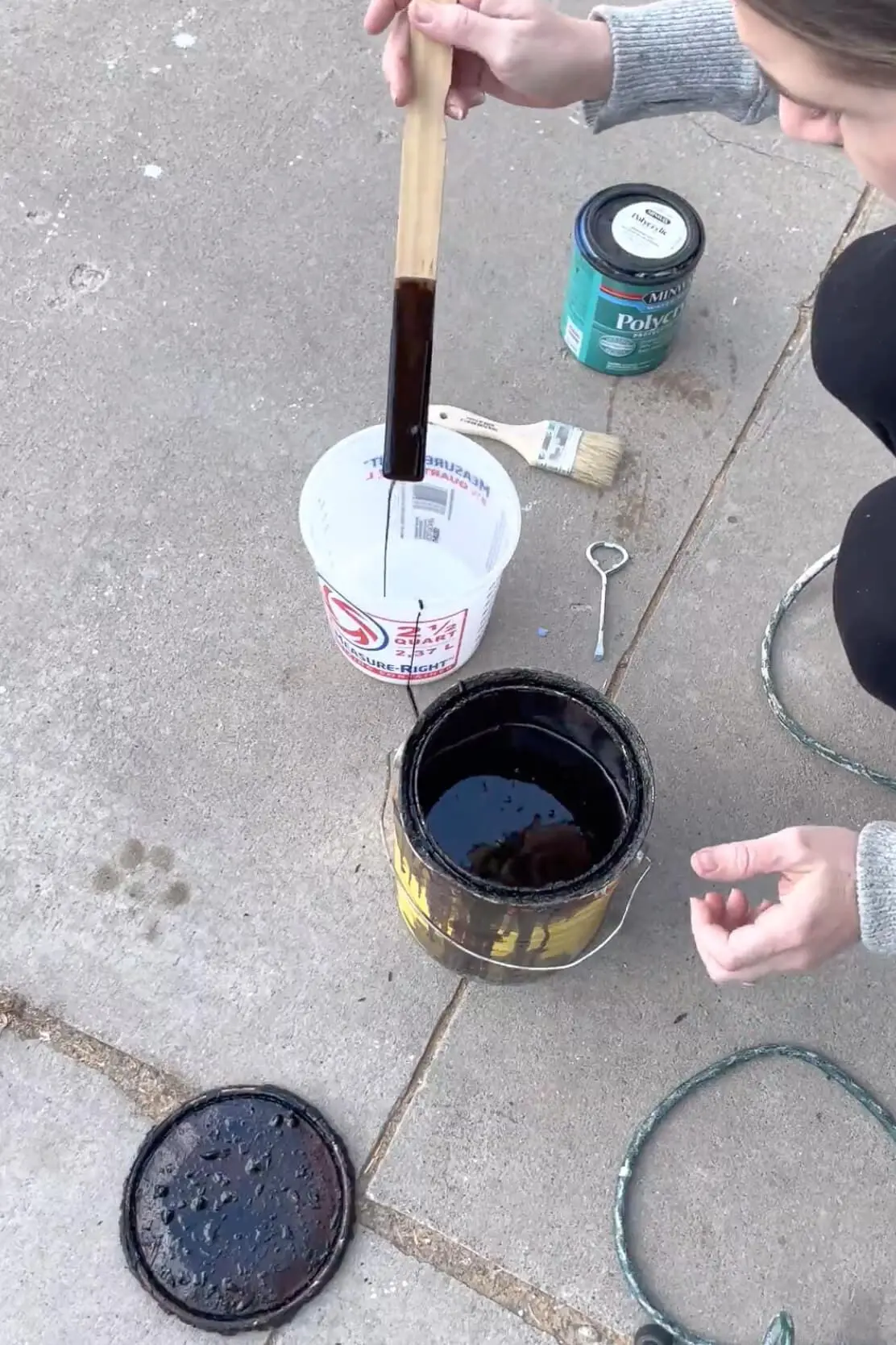 A close-up of a DIY wood finishing project, stirring dark stain in a measuring cup with polycrylic.